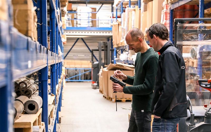 Twee medewerkers scannen producten in een magazijn van Van Buuren Groep