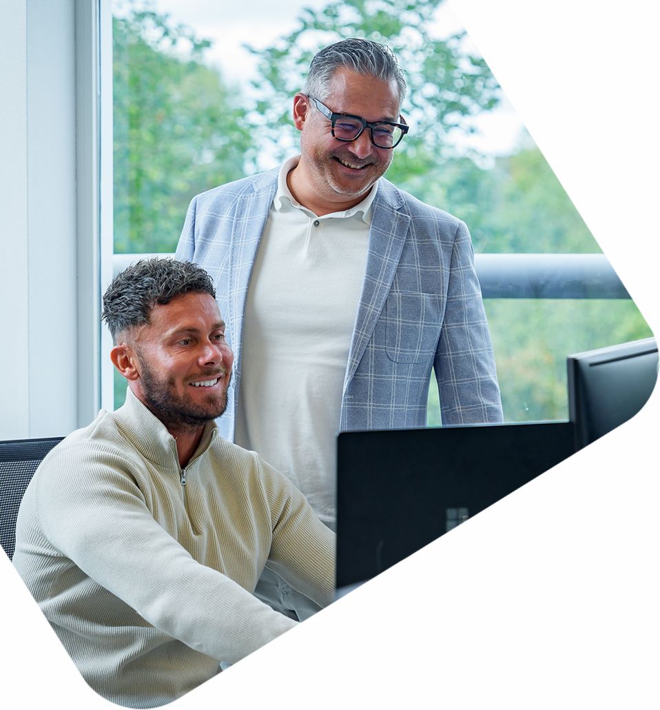 Twee collega’s van een e-commerce bureau overleggen lachend achter computerscherm in modern kantoor