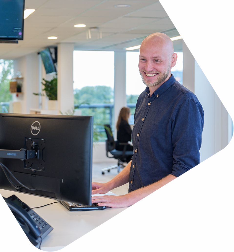 Man achter bureau glimlacht bij monitor, kantoren op de achtergrond